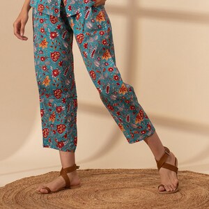 May include: Teal blue trousers with a floral print in shades of red, orange, and white. The trousers are cropped and have a wide leg.