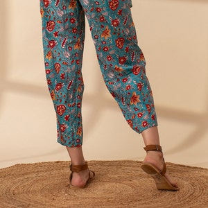 May include: Teal blue trousers with a floral print in shades of red, orange, and white. The trousers are cropped and have a wide leg.