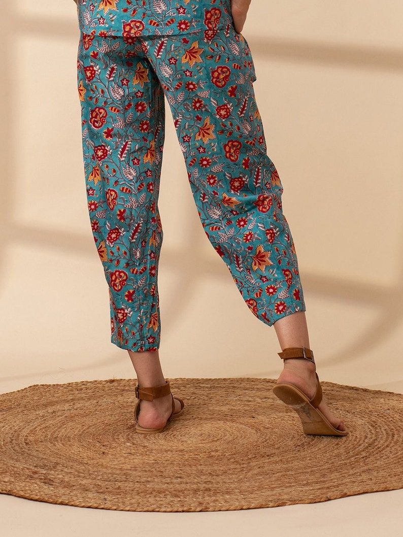 May include: Teal blue trousers with a floral print in shades of red, orange, and white. The trousers are cropped and have a wide leg.
