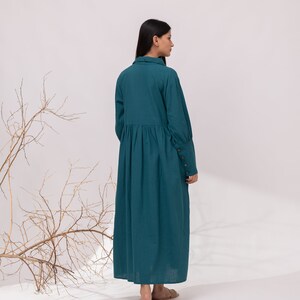 May include: A teal blue long-sleeved dress with a collared neckline and a gathered skirt. The dress has button details on the cuffs.