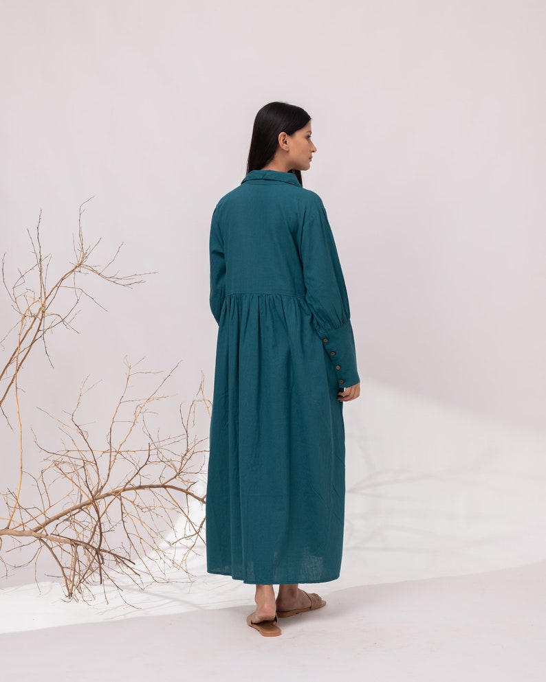 May include: A teal blue long-sleeved dress with a collared neckline and a gathered skirt. The dress has button details on the cuffs.
