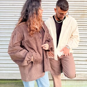 Puede incluir: Dos personas con chaquetas y pantalones de pana. Una persona lleva una chaqueta de pana marr&oacute;n con vaqueros azul claro. La otra persona lleva una camisa color crema y pantalones de pana marrones. Ambos llevan gafas de sol.