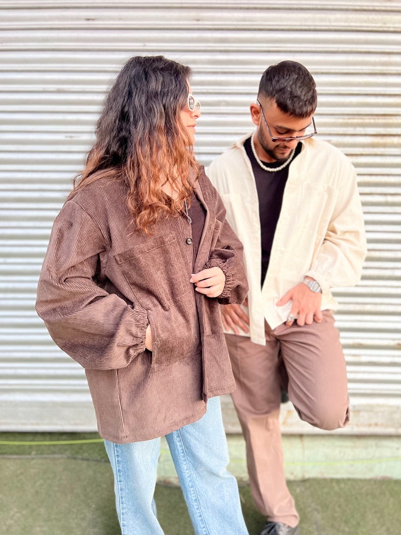 Puede incluir: Dos personas con chaquetas y pantalones de pana. Una persona lleva una chaqueta de pana marr&oacute;n con vaqueros azul claro. La otra persona lleva una camisa color crema y pantalones de pana marrones. Ambos llevan gafas de sol.