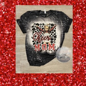 May include: Black t-shirt with a bleached design and a graphic of a young cheerleader in a red and white uniform. The words "Cheer MOM" are printed in red and white script.