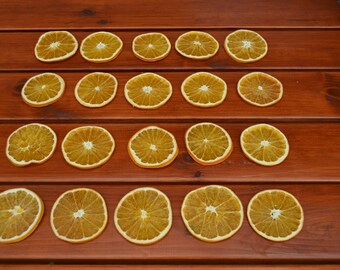 May include: A top-down shot displays dried orange slices, neatly arranged in rows on a dark brown wooden surface. The circular slices are light brown, with visible segments, creating a natural, rustic aesthetic.