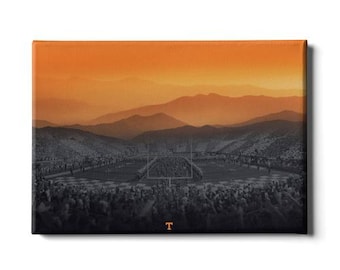 May include: Canvas art print featuring a football stadium scene with a vibrant orange and black color scheme. The image depicts a stadium filled with spectators, set against a backdrop of layered mountains under an orange sky. A letter "T" is visible.