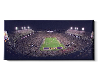 May include: A panoramic view of a packed football stadium at night. The field is lit up with bright lights, and the stands are filled with cheering fans. The stadium is surrounded by a dark sky, and the lights of the city can be seen in the distance. The words "LSU" are visible on the field.