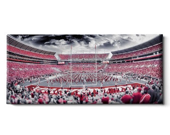 May include: Panoramic view of a football stadium filled with spectators. The stands are packed with fans wearing red. The field features a marching band performing. The sky is overcast with dark clouds.