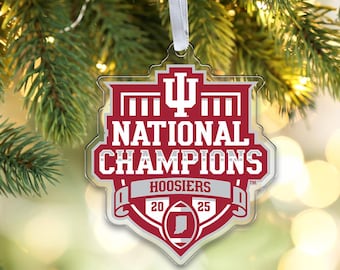 Może przedstawiać: Przezroczysta ozdoba z akrylu w kształcie tarczy z bordowo-białym wzorem, zawierająca napis National Champions Hoosiers 2025, logo Indiana University oraz grafikę piłki do futbolu amerykańskiego z sylwetką stanu Indiana.