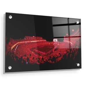 May include: A panoramic view of a packed football stadium at night. The stadium is filled with fans wearing red, and the field is lit up with bright lights. The words "Bulldogs" are visible on the field.