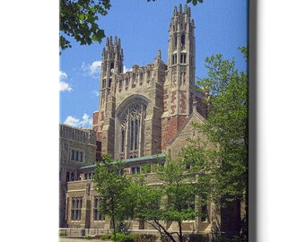 May include: A canvas print of a large stone building with two tall towers and a large arched window. The building is framed by green trees and a blue sky with clouds. The architecture features intricate details and a mix of stone and brick.