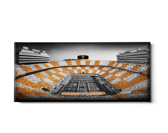 May include: A black and white photograph of a football stadium with orange and white checkered seats. The stadium is full of fans and the field is visible in the center. A large scoreboard with a "T" on it is visible in the background.