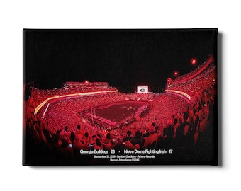 May include: A night game at Sanford Stadium in Athens, Georgia, with a packed crowd of fans in red. The scoreboard shows the Georgia Bulldogs defeating the Notre Dame Fighting Irish 23 to 17. The text below the scoreboard reads "September 21, 2019 - Sanford Stadium - Athens Georgia" and "Record Attendance 93,246".