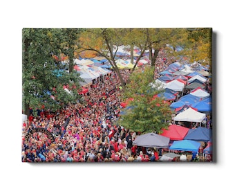 May include: A large crowd of people gathered under a canopy of trees and colorful tents. The crowd is wearing red and blue clothing, and there are many flags and banners in the background. The text "Walk of Champions" is visible in the lower left corner of the image.