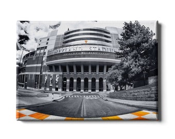 Puede incluir: Una fotografía en blanco y negro del Neyland Stadium, hogar del equipo de fútbol americano de los Volunteers de la Universidad de Tennessee. El estadio es una gran estructura moderna con una entrada de arco distintiva. La foto está tomada desde un ángulo bajo, dando al espectador una sensación de la grandeza del estadio.