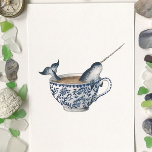 May include: A watercolor illustration of a narwhal swimming in a blue and white teacup. The narwhal is depicted with a long, spiraled tusk and a gray body. The teacup is decorated with a floral pattern.