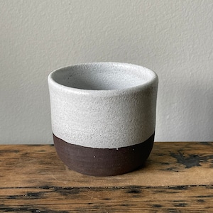 May include: A white ceramic mug with a brown rim. The mug has a speckled white glaze and a smooth brown glaze on the rim.