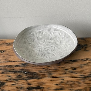 May include: A white ceramic bowl with a textured, geometric pattern. The bowl has a dark grey rim and is sitting on a wooden surface.