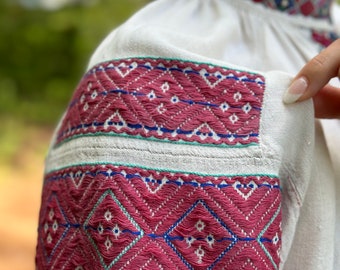 May include: White linen shirt with embroidered details in pink, blue, and green. The embroidery features a geometric pattern of diamonds and zigzags.