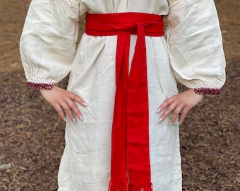 May include: A white linen dress with embroidered sleeves and a red sash. The dress has a V-neckline and a loose fit. The sash is tied at the waist and has long tassels.