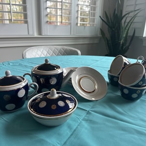 Puede incluir: Un juego de té azul y blanco con detalles dorados. El juego incluye una tetera, una jarra de crema, un azucarero, cuatro tazas y cuatro platillos. Las tazas y los platillos tienen un patrón floral azul y blanco con detalles dorados.