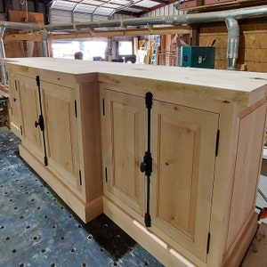 May include: A light wood cabinet with two sets of double doors. Each door has a black metal handle and a black metal hinge. The cabinet is sitting on a black surface.
