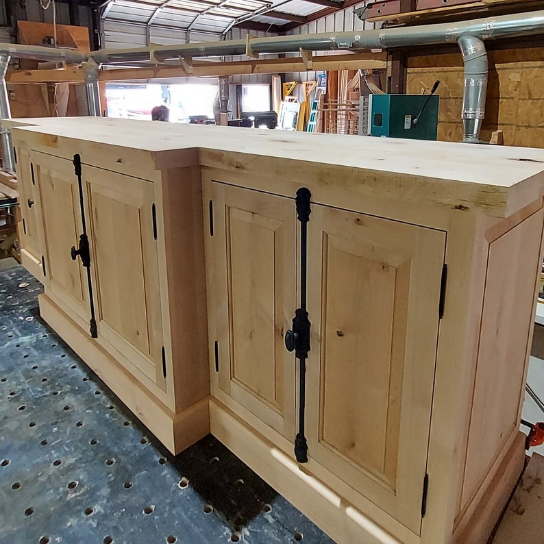 May include: A light wood cabinet with two sets of double doors. Each door has a black metal handle and a black metal hinge. The cabinet is sitting on a black surface.