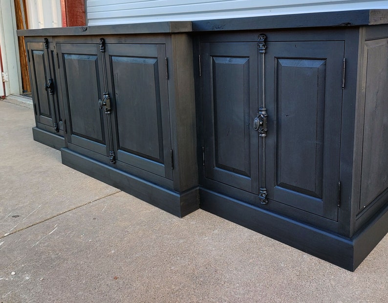 May include: A black wooden cabinet with four doors and ornate metal hardware. The cabinet has a dark wood finish and a simple design.