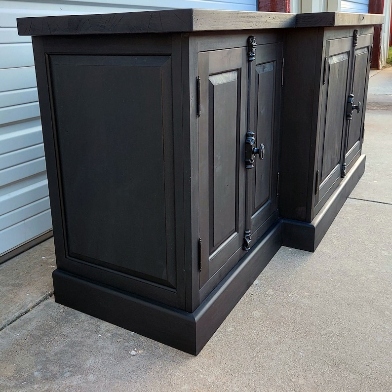 May include: A black wooden cabinet with two sets of double doors. The cabinet has a dark wood finish and black hardware. The cabinet is sitting on a concrete floor.