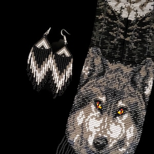 Op de afbeelding: Een paar zwarte en witte kralen oorbellen met een kralenontwerp van een wolfskop. De wolf heeft oranje ogen.