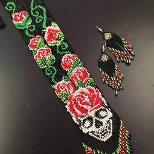 May include: A long black beaded necklace with a skull and red roses design. The necklace has a fringe of beads and comes with matching earrings.