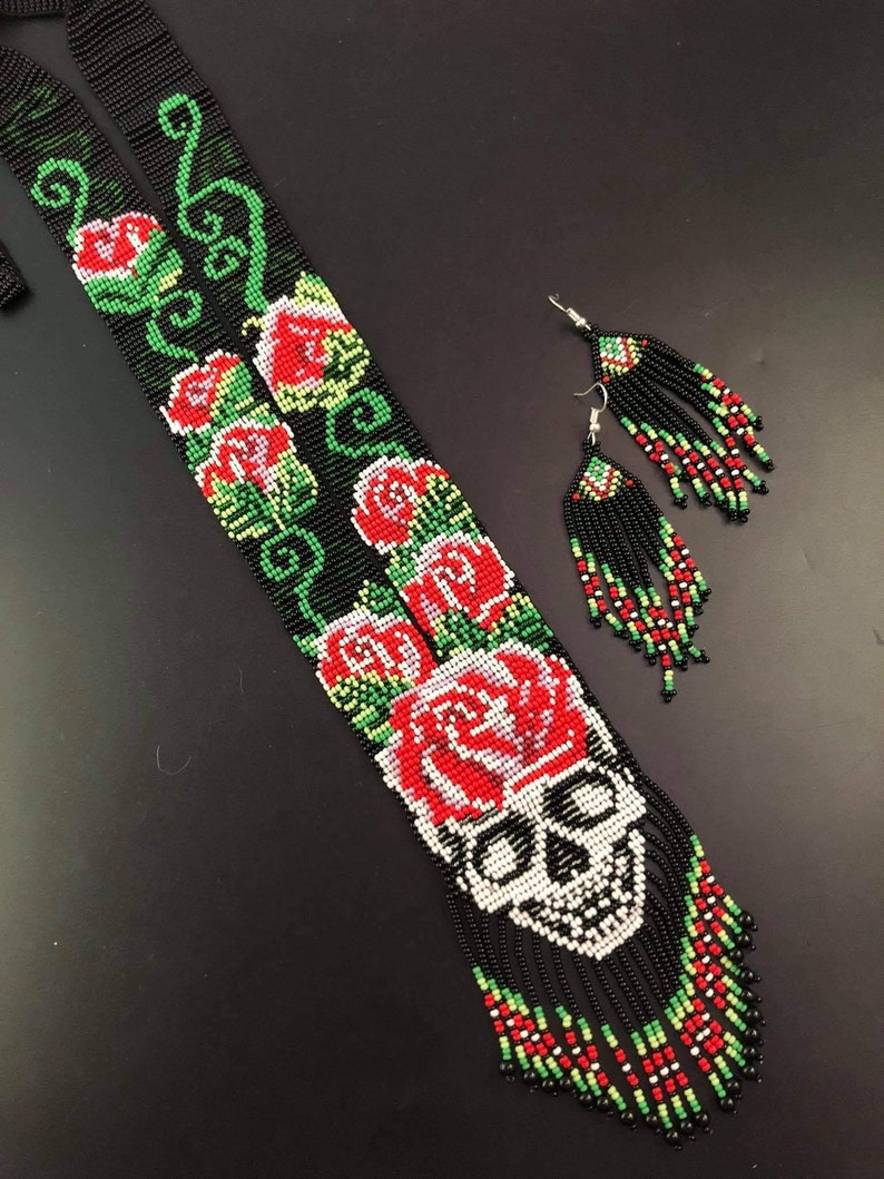 May include: A long black beaded necklace with a skull and red roses design. The necklace has a fringe of beads and comes with matching earrings.