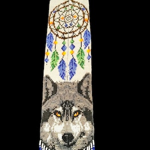 May include: A white beaded necklace featuring a wolf face and a dreamcatcher design. The necklace has blue and white fringe.