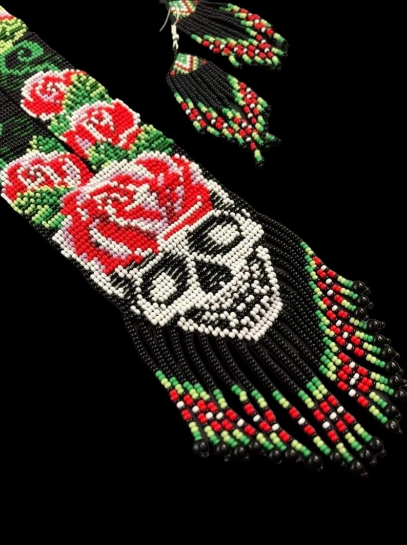 May include: A pair of beaded earrings with a skull and roses design. The earrings are black with red, white, and green beads. The skull is white with black details. The roses are red with white and green details.