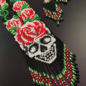 May include: A beaded necklace and earrings set with a skull design and red roses. The necklace has black, white, red, and green beads. The earrings are black, white, red, and green with black tassels.