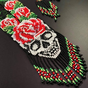 May include: A beaded necklace and earrings set with a skull design, red roses, and black, white, green, and red beads.