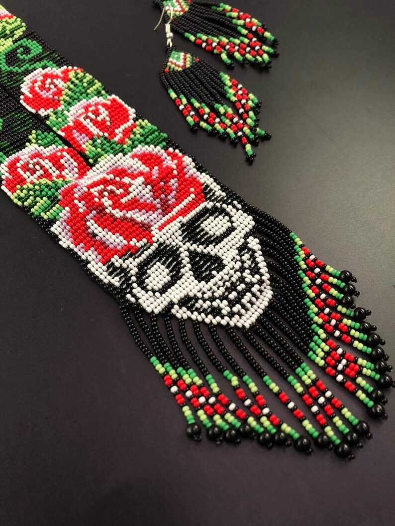 May include: A beaded necklace and earrings set with a skull design, red roses, and black, white, green, and red beads.