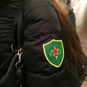 May include: A black puffer jacket with a green and yellow patch featuring a red star and the letters "YJP".