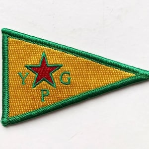 May include: A yellow triangular flag with a green border. A red star is in the center with the letters "YPG" in white.