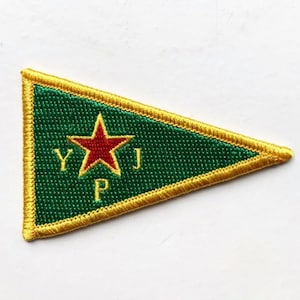 May include: A green triangular patch with a yellow border. A red star with a yellow outline is in the center of the patch. The letters YPJ are embroidered in yellow below the star.
