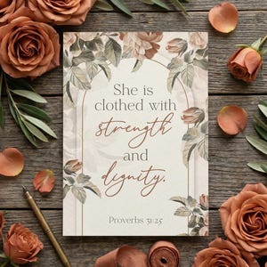 May include: A floral-themed image featuring a card with the text "She is clothed with strength and dignity." The card is surrounded by rust-colored roses, olive branches, and a ribbon on a wooden surface. A gold pen is also present.