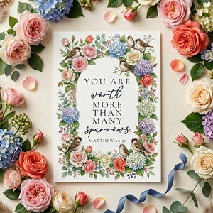 Könnte beinhalten: Ein floraler Druck mit dem Text "YOU ARE worth MORE THAN MANY sparrows." umgeben von Rosen, Hortensien und kleinen Vögeln. Die Farbpalette umfasst Rosa-, Blau- und Cremetöne, mit einem blauen Band und verstreuten Blütenblättern.