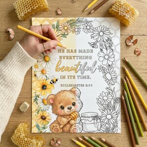May include: A coloring page with the text "He has made everything beautiful in its time." and a teddy bear holding honey. The page is surrounded by daisies, bees, and honeycombs. Colored pencils are scattered around the page.
