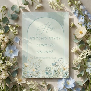 Könnte beinhalten: Ein rechteckiger Druck mit dem Text "His mercies never come to an end" in eleganter Schrift, umgeben von einem sanften grünen Bogen und floralen Illustrationen. Der Druck wird von einer Anordnung weißer, blauer und grüner Blumen und Blätter umrahmt.