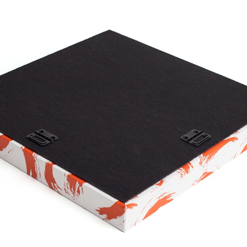 May include: A square canvas art piece with a black backing and two metal hanging brackets. The sides of the canvas are white with orange brushstroke designs. The artwork is ready to hang.
