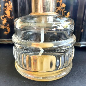 May include: A clear glass bottle with a gold top and a textured base. The bottle is filled with a clear liquid and has a white wick inside.