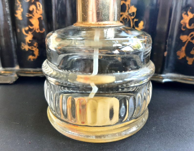 May include: A clear glass bottle with a gold top and a textured base. The bottle is filled with a clear liquid and has a white wick inside.