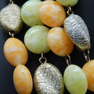May include: A multi-strand necklace with alternating light green, white and orange oval beads and silver-toned beads with a textured surface.