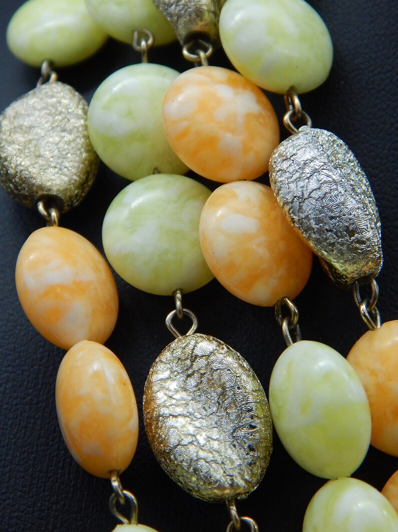 May include: A multi-strand necklace with alternating light green, white and orange oval beads and silver-toned beads with a textured surface.