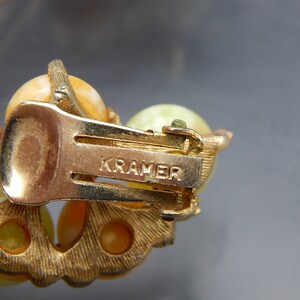 May include: Gold tone clip-on earrings with a cluster of yellow and green stones. The back of the earrings are marked "KRAMER".